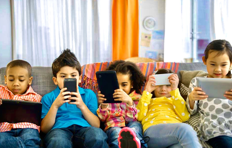 children on a couch using screen devices